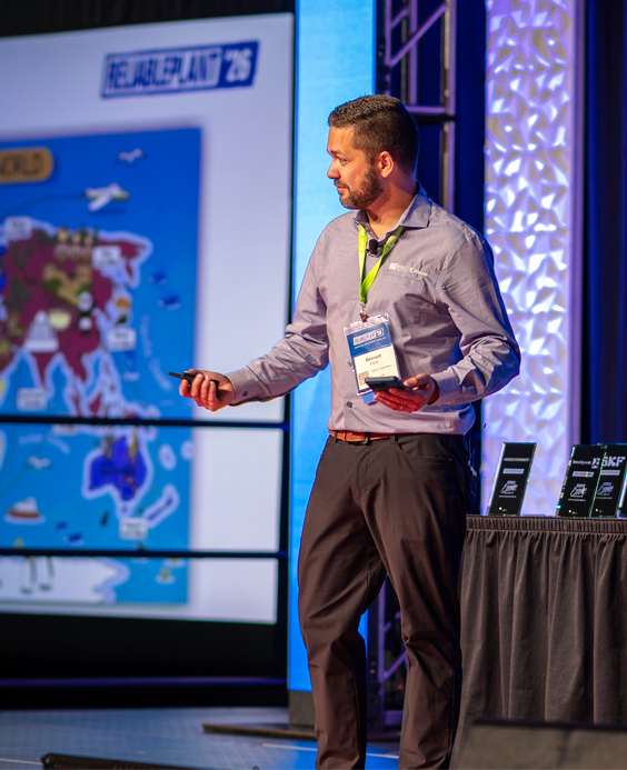 A speaker presenting on stage during a Reliable Plant conference session.